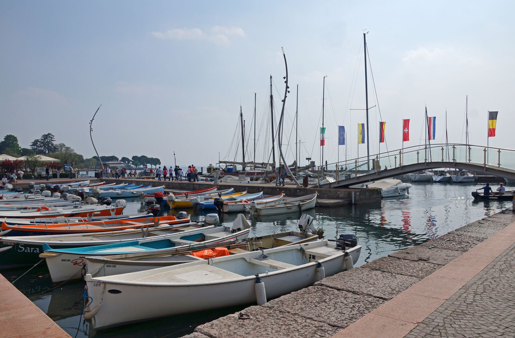 Sommerlicher Hafen von Bardolino mit bunten Holzbooten und einer geschmückten Bogenbrücke